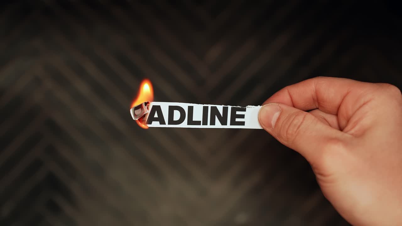 Close-up hand burning a paper label reading “DEADLINE” with flame on dark background, stress and urgency concept, copy space