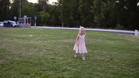 Glückliche-Mutter-Mit-Langen-Blonden-Haaren-Lacht,-Während-Sie-Ihr-Kleines-Mädchen-In-Zeitlupe-Durch-Einen-Grünen-Park-Huckepack-Trägt