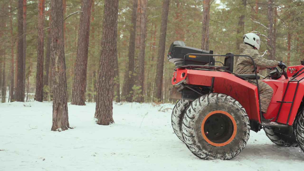 Pilota di ATV che lascia un sentiero innevato tra i pini su un quad rosso, figura con casco passa accanto ai tronchi d'albero in una foresta invernale deserta, inquadrature ampie mostrano un paesaggio innevato e silenzioso, atmosfera calma e contemplativa di viaggio