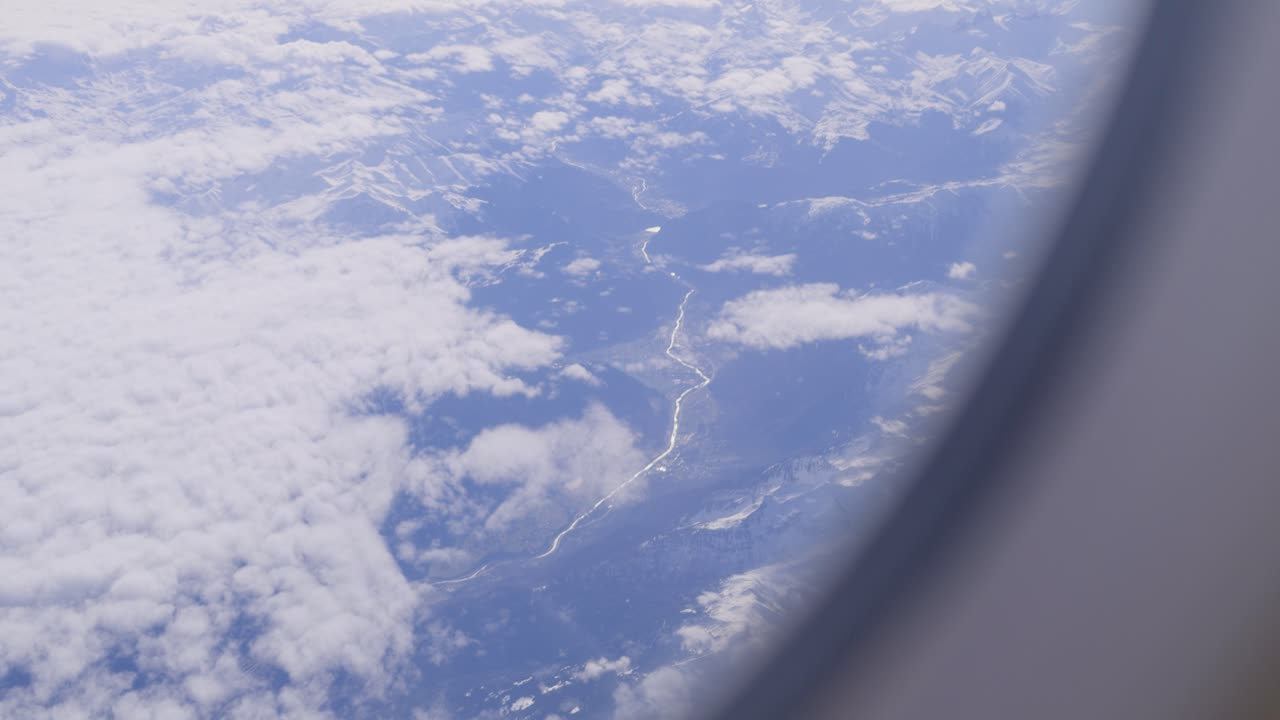 Winding river, snowy peaks, and clouds seen from airplane window, aerial view