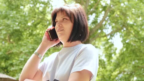 atractiva mujer de buen aspecto con cabello negro cortado hablando por teléfono en el bosque