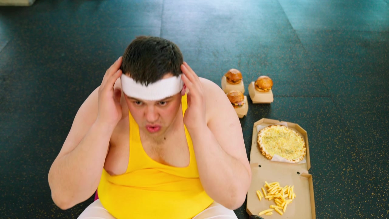 Uomo in sovrappeso che fatica con gli addominali mentre è tentato dal fast food