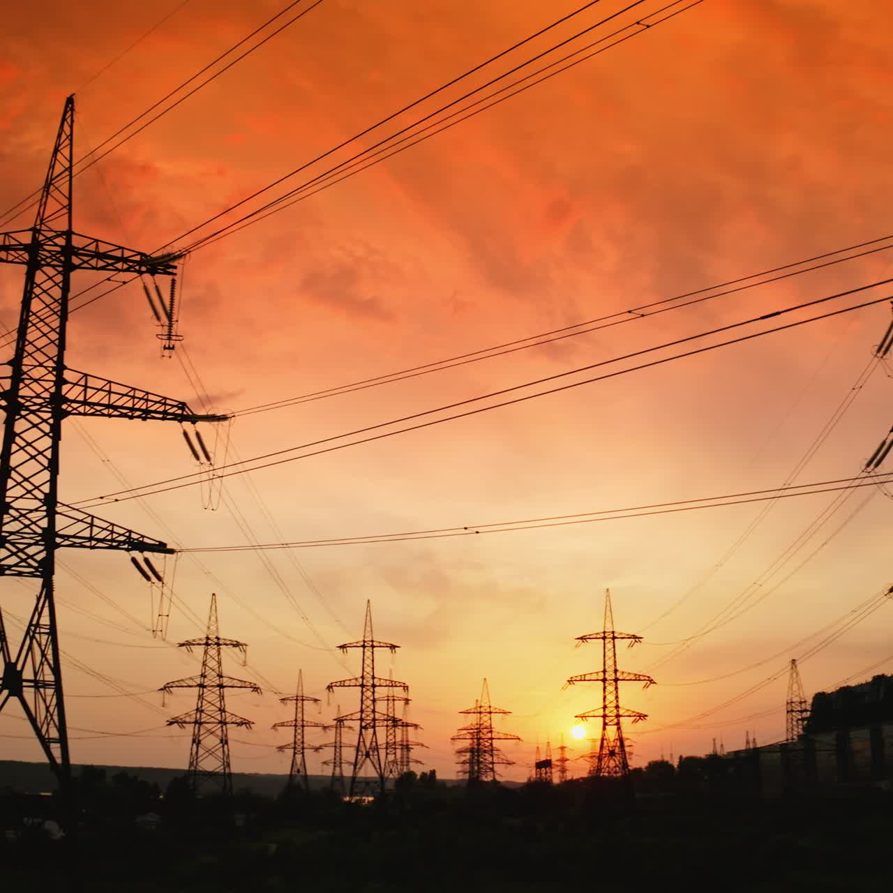 Electrical pylons near harmful factory at red sunset. Dark smoke released into the air from industrial pipe. Transmission lines. Pollution the environment. Camera moving down