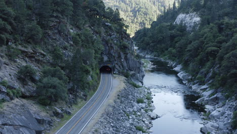 aerial following car on canyon road entering dark tunnel through rocky mountain