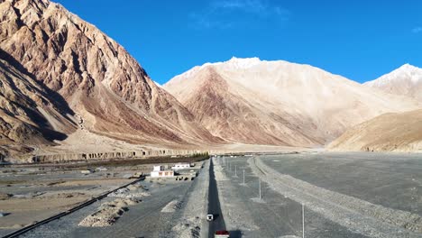 aerial drone shot of a car crossing a dry riverbed in ladakh, leaving a trail of dust behind.