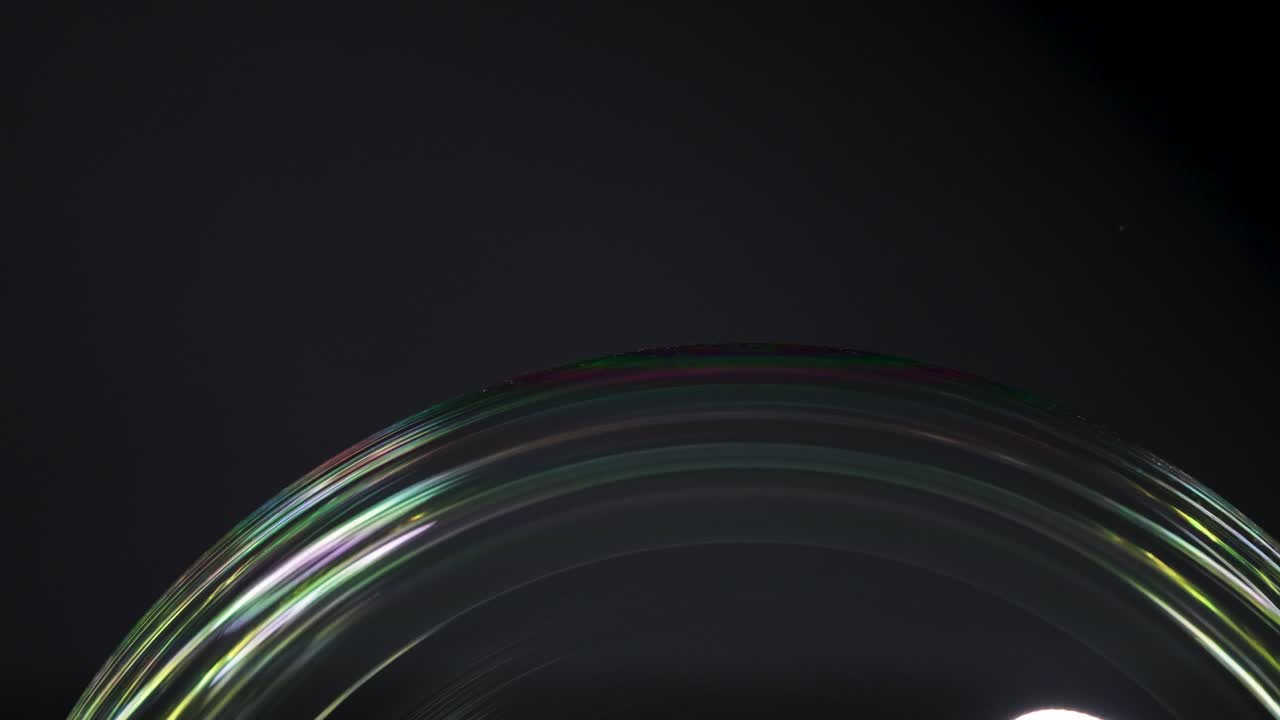 Close-up video of a soap bubble showing dynamic color reflections under soft lighting