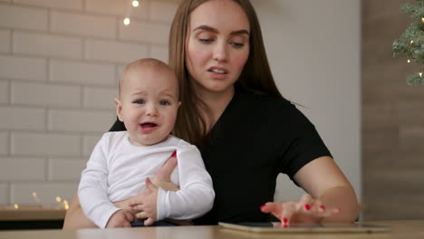 y mamá y bebé sentados en la mesa jugando a la tableta presionando los dedos en la pantalla y riendo