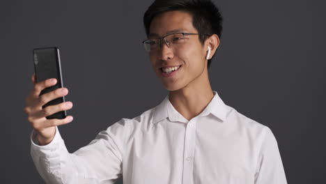 Asiatischer-Mann-Mit-Kopfhörern,-Der-Einen-Videoanruf-Auf-Dem-Smartphone-Führt.