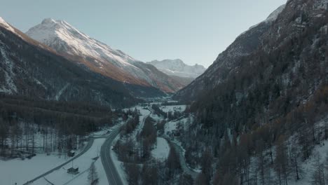 Aufsteigende-Luftaufnahme-Durch-Flusstal-In-Epischen-Schweizer-Alpen-Mit-Atemberaubendem-Alpengebirgspanorama-Und-üppigen-Kiefernwäldern-An-Hängen