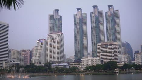 Skyscraper-view-of-tall-buildings-from-Benjakitti-Park-in-the-city-of-Bangkok,-Thailand-handheld-dynamic