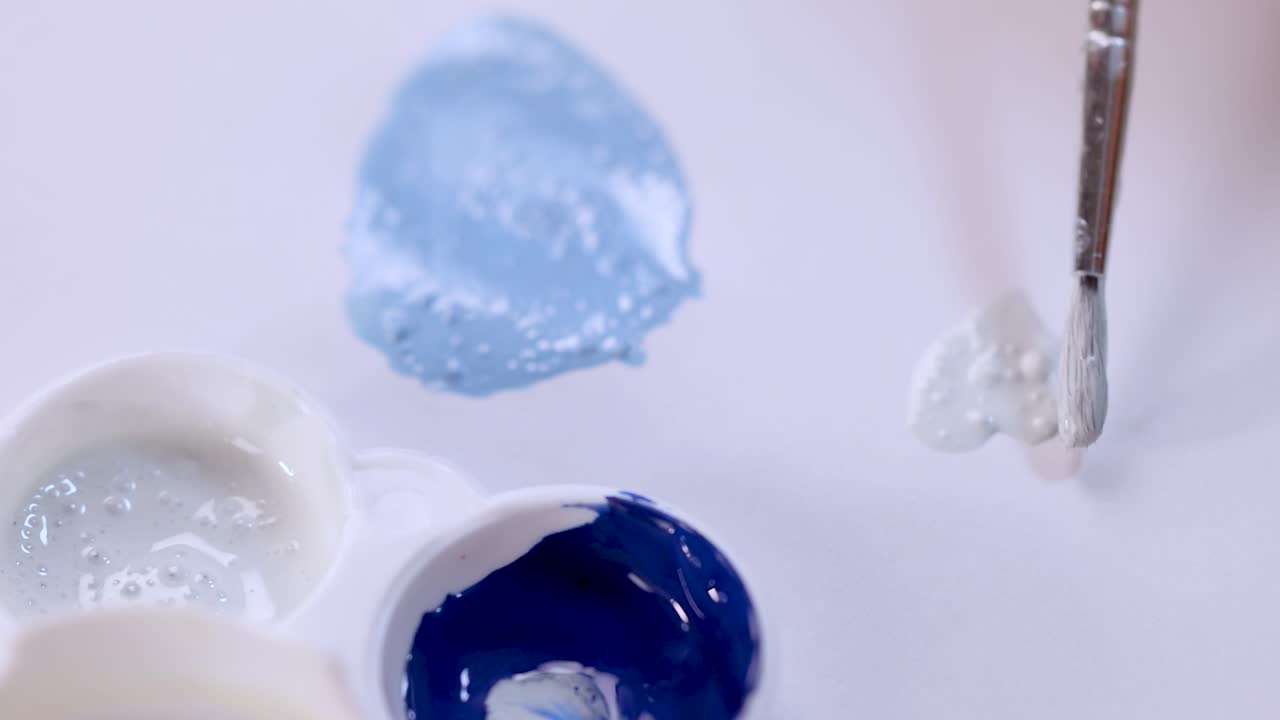 Hand dips brush in white paint, mixes on palette under soft lighting, smooth motion