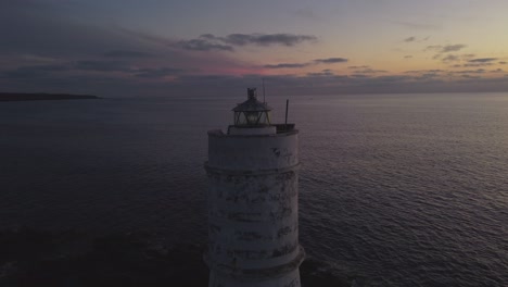 Establisher-shot-of-magical-solitary-lighthouse-shining-light-at-dusk,-dolly-out