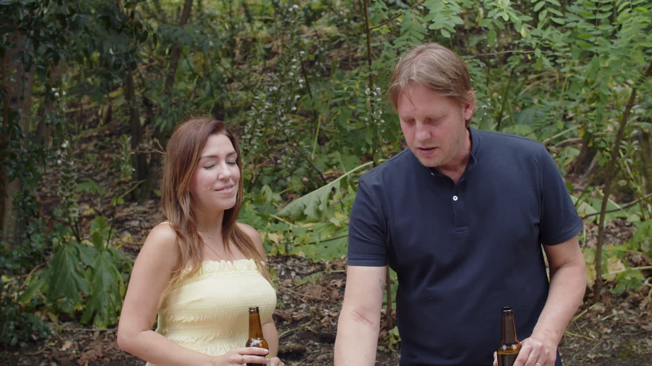 맥주 병을 들고 서서 음식을 굽고 있는 행복한 백인 커플