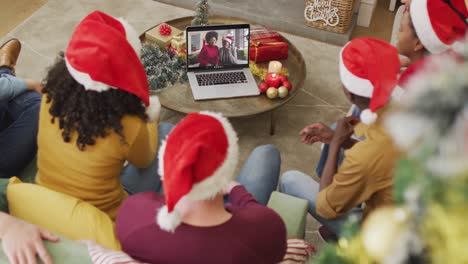 Vielfältige-Familie-Mit-Weihnachtsmützen-Und-Laptop-Für-Weihnachtsvideoanruf-Mit-Glücklicher-Familie-Auf-Dem-Bildschirm