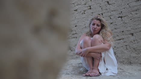 Panning-reveal-shot-of-a-woman-in-a-white-dressed-crouched-amongst-old-Greek-ruins