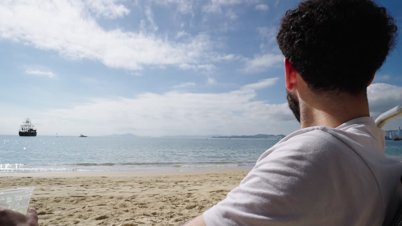 Man sitting on sandy beach relaxing while drinking Caipirinha cocktail overlooking the calm ocean environment