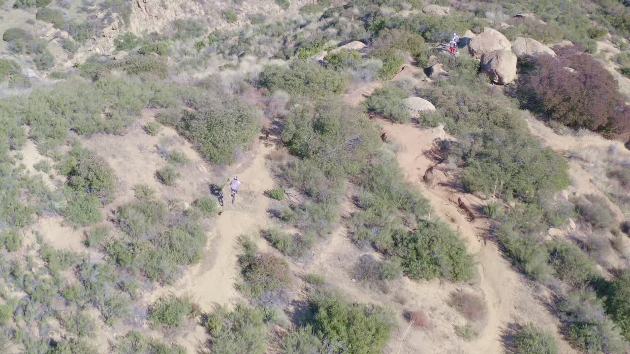 Offroad mountain bikers jumping dirt ramps by drone