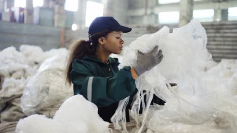 and-African-American-woman-in-a-special-uniform-sorts-polyethylene-at-a-waste-recycling-plant.-Processing-of-raw-materials