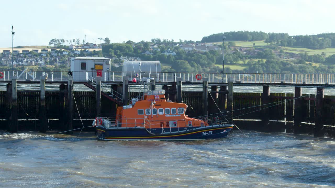 An orange lifeboat is secured at a pier amid choppy waves in Broughty Ferry