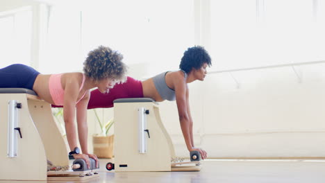 dos mujeres biraciales, una joven y una madura, haciendo ejercicio en máquinas de pilates
