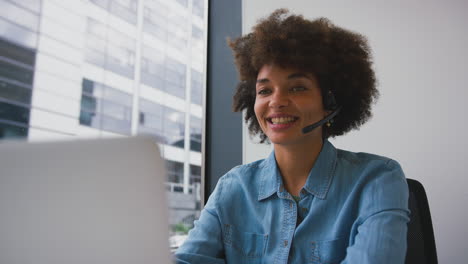 Junge-Geschäftsfrau-Im-Modernen-Büro,-Die-Mit-Einem-Drahtlosen-Headset-Am-Laptop-Arbeitet