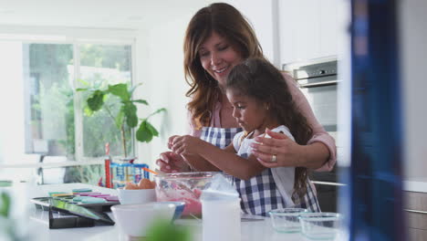 hispanic grandmother and granddaughter having fun in kitchen making cake together