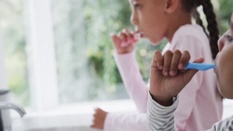 hermano y hermana bi-raciales felices cepillándose los dientes en un baño soleado, cámara lenta
