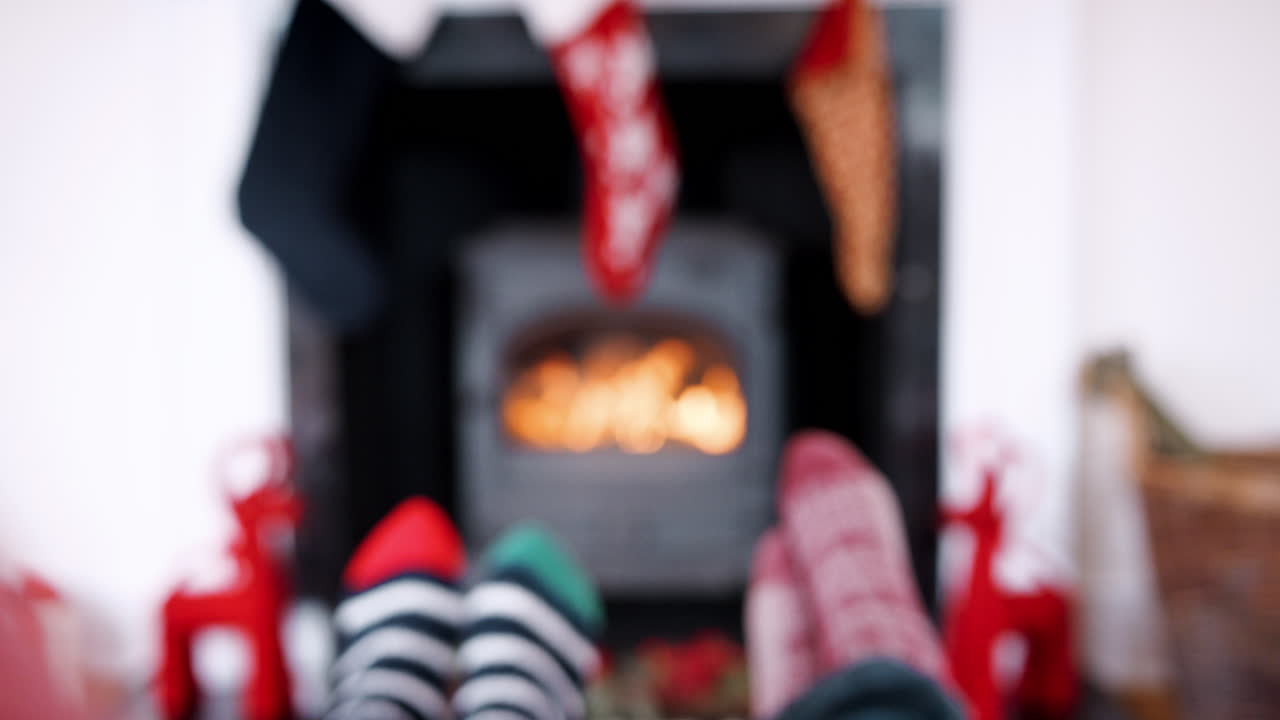 Low section of couple&rsquo;s feet in front of a fireplace,  hands raising their glasses to make a toast, detail