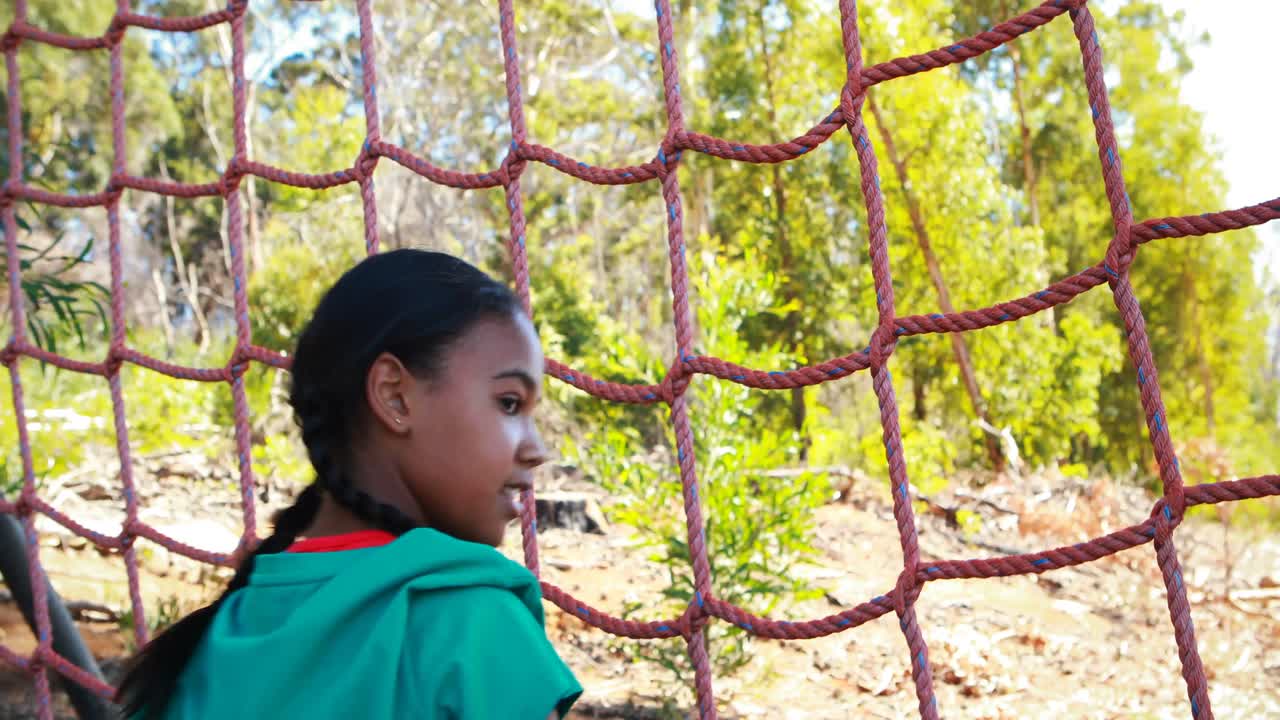 chica feliz animando durante la escalada de la red en el campamento de entrenamiento