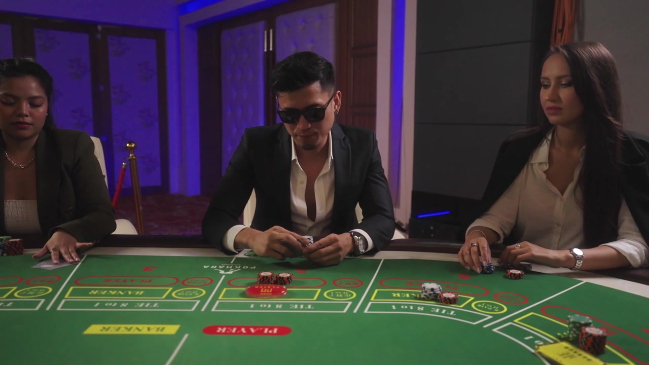 Filmato cinematografico di casinò che mostra uomini e donne riuniti attorno a un tavolo da gioco, che partecipano a una vivace esperienza di gioco da casinò circondati da interni di lusso e illuminazione suggestiva