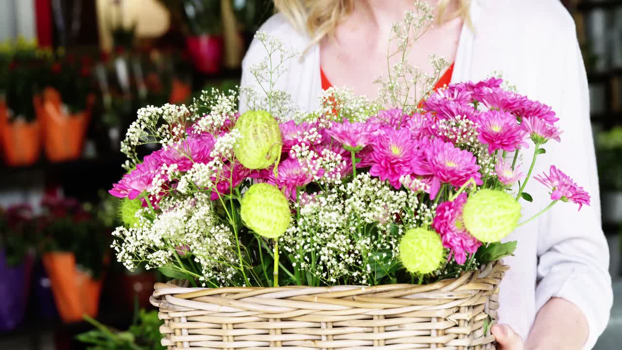 sección media de florista femenina sosteniendo un ramo de flores en una floristería