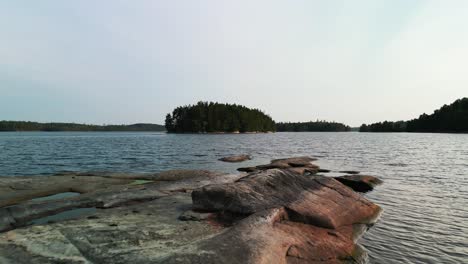 Aerial-of-low-pass-over-rocks-toward-lake-islands,-Sweden