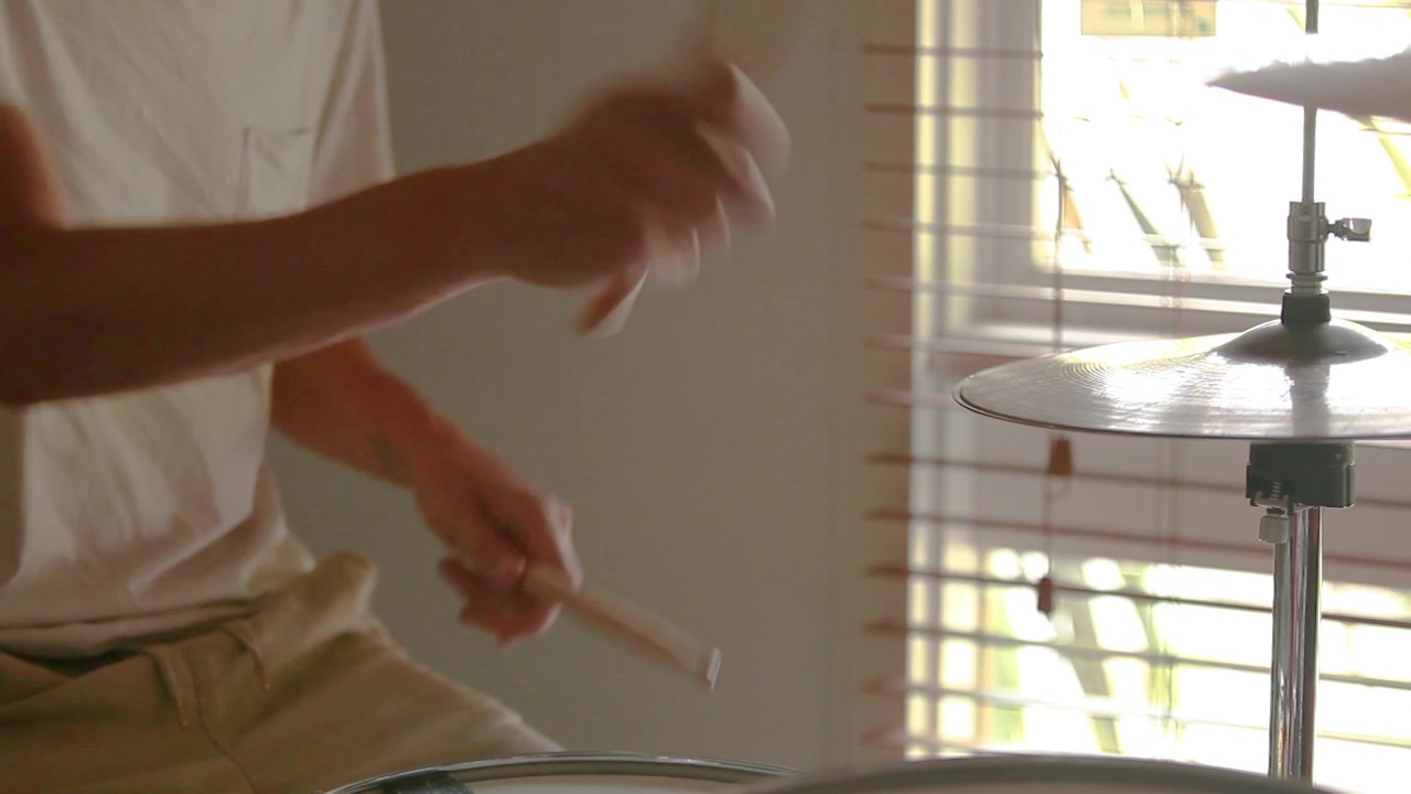 Drummer practicing rudiments on his home drum kit with natural light coming through window glass.