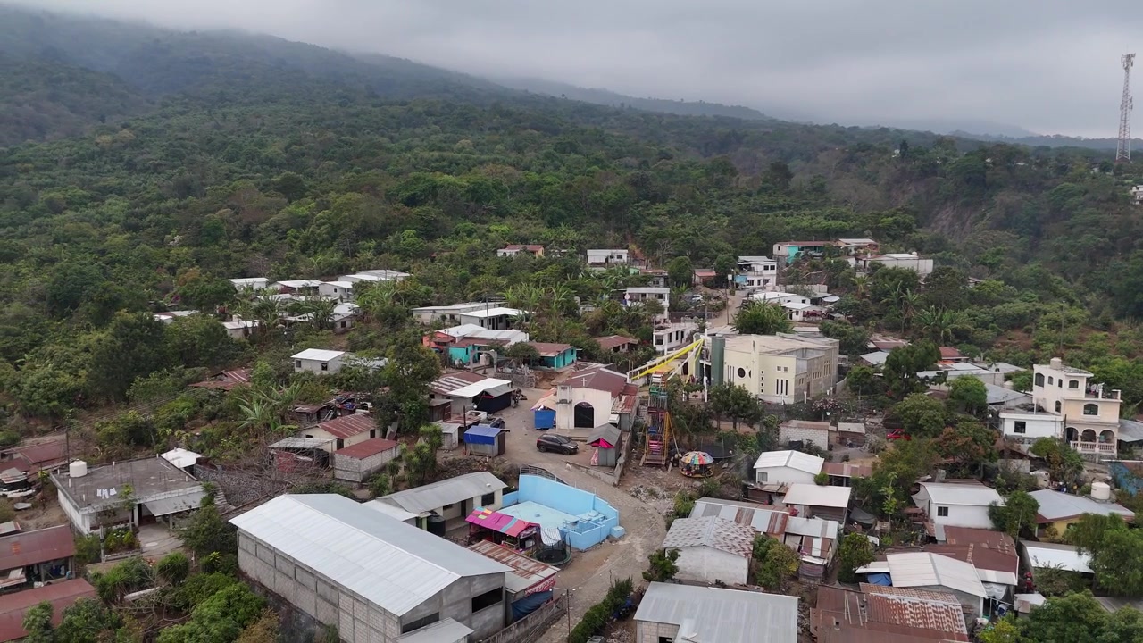 En filmatisk dronevideo fra San Lucas Guatemala fanger tropiske nabolag, livlige hus, frodige palmetrær og skogkledde fjellbakgrunner for en fantastisk luftutsikt over Mellom-Amerika.