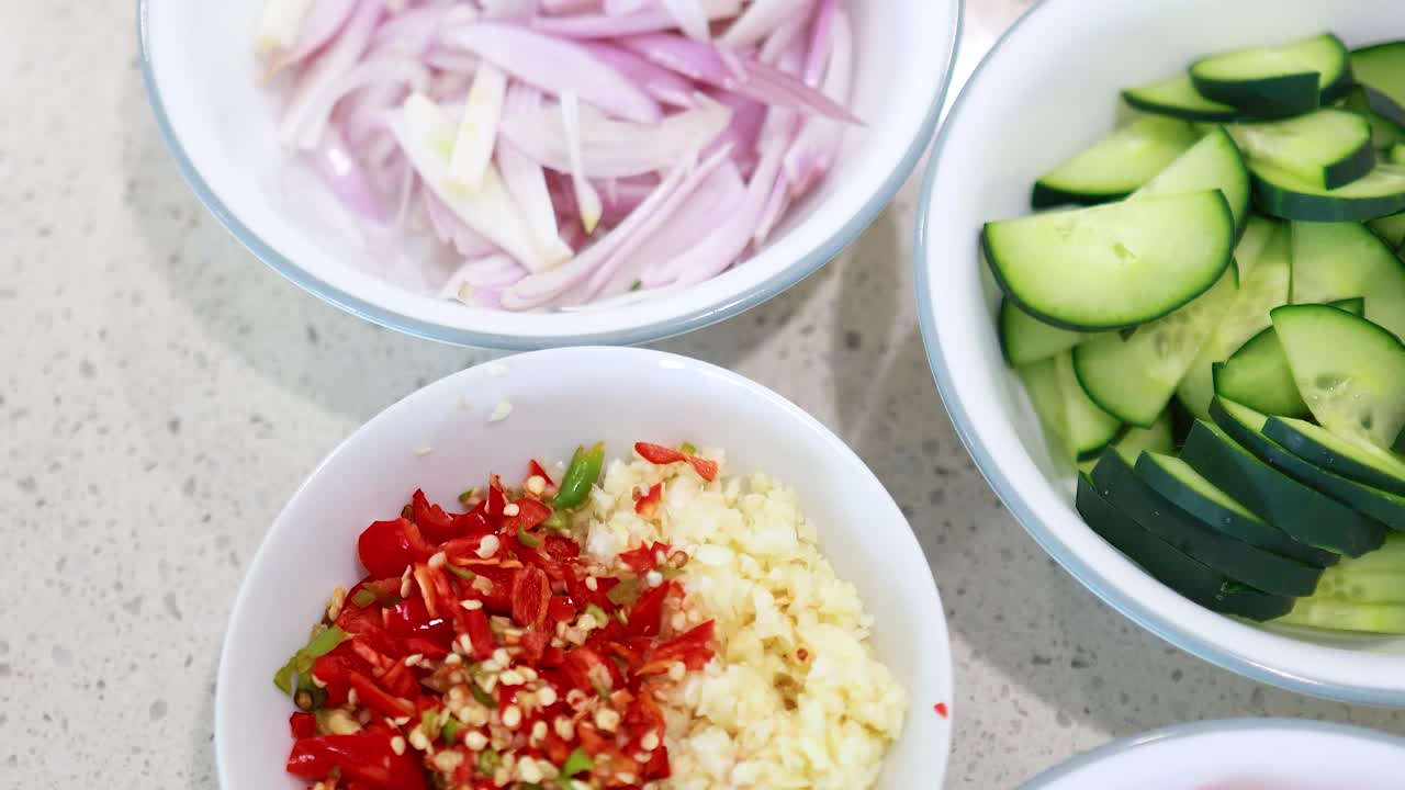 Chopped tomatoes, cucumbers, shallots, and chilies on a kitchen counter under bright lighting