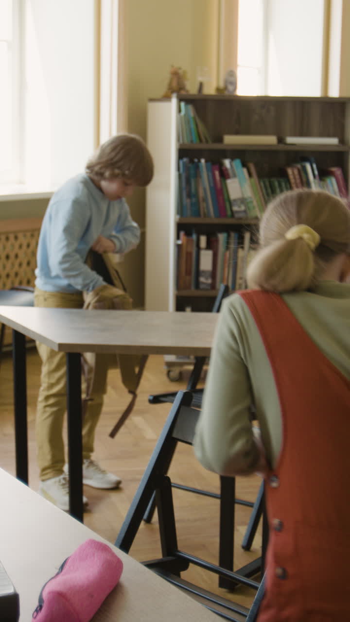 Children packing their backpacks at desks in a classroom