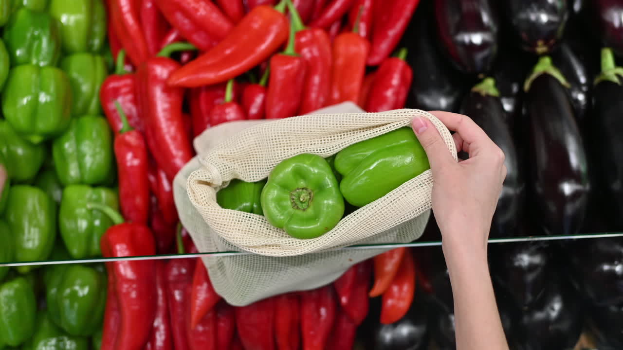 Woman picking bell peppers in a reusable bag in a store. Ecology and Earth Day thematics. Slow motion