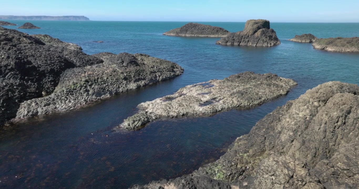 Piccole isole rocciose che circondano il porto di Ballintoy con acqua cristallina color turchese.