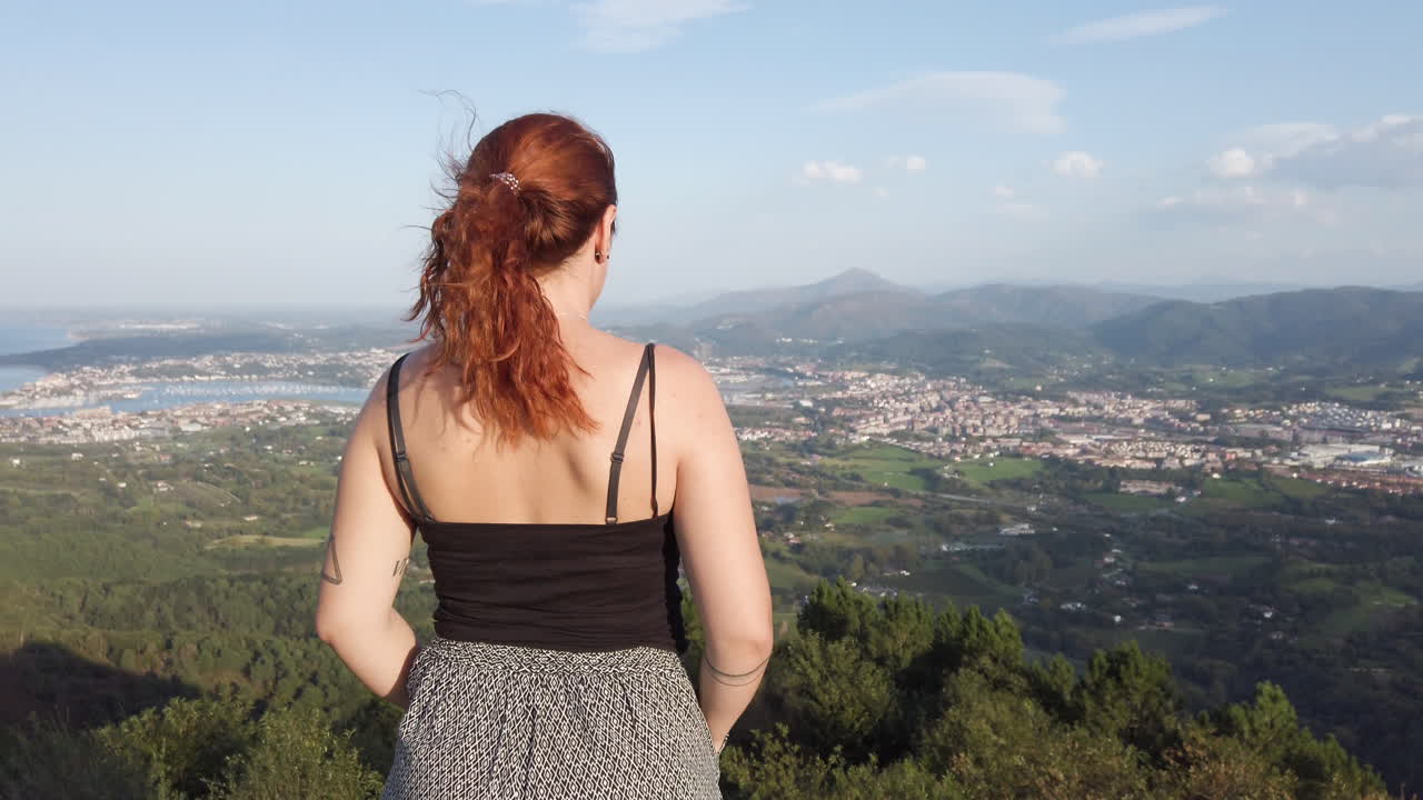 Woman with red hair overlooking a city and mountains