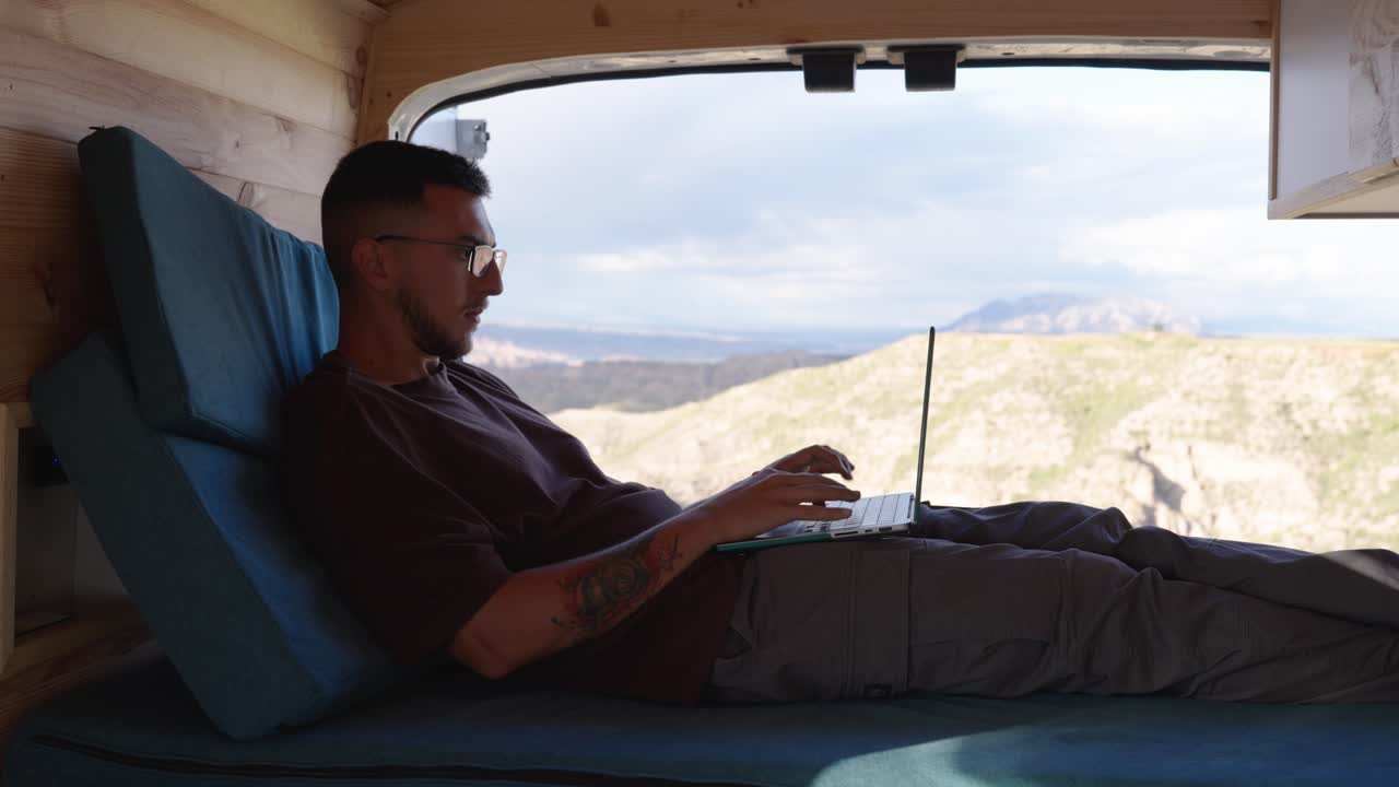 Digital nomad working on netbook from campervan with scenic mountain view