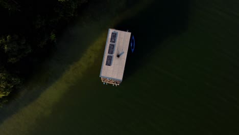 Top-down-shot-of-a-house-boat-floating-on-a-lake-next-to-a-forest-in-Brandenburg,-Germany