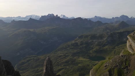 aerial view of rugged mountain landscape with steep cliffs and green valleys, featuring the gross achslenstock in the distance, under a clear sky with distant snow-capped peaks