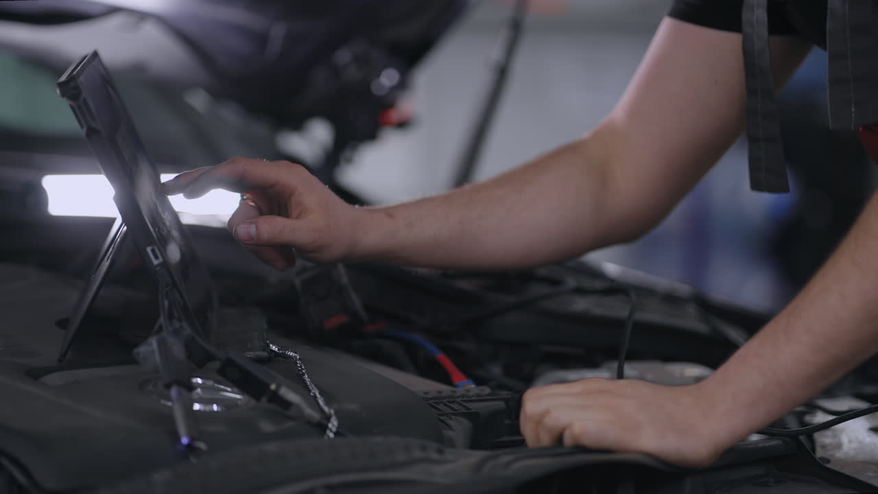 primer plano en el capó del coche un mecánico con una tableta presiona la pantalla para diagnosticar problemas