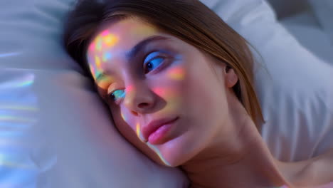 woman lying in bed with colorful light reflections on her face