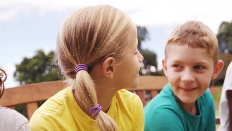 Kids-interacting-with-each-other-sitting-on-bench-in-park