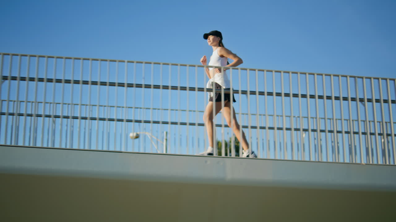 Athletic woman running bridge in front clear blue sky. Energetic lady jogging