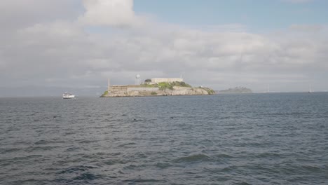 alcatraz island in the distance with a boat sailing next to it with san francisco in the background