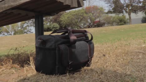 una pequeña bolsa de cámara dejada en el césped debajo de un banco de madera