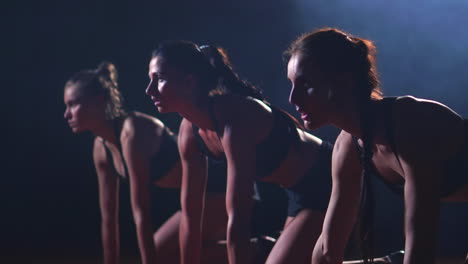 three girls in black clothes are in the starting pads to start the race in the competition in the light of the lights and run towards the finish