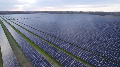 aerial establishing shot of large photovoltaic solar panel farm installed in green field in rural area during cloudy day